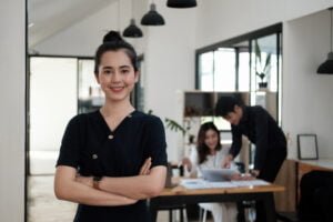 Confident woman standing in modern office with colleagues working in background