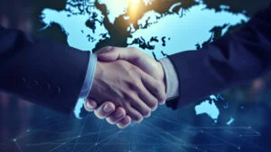 Two business professionals shaking hands in front of a digital world map symbolising international recruitment partnerships.